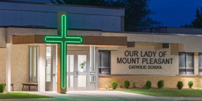 Our Lady of Mount Pleasant School exterior front entrance with cross glowing green at night