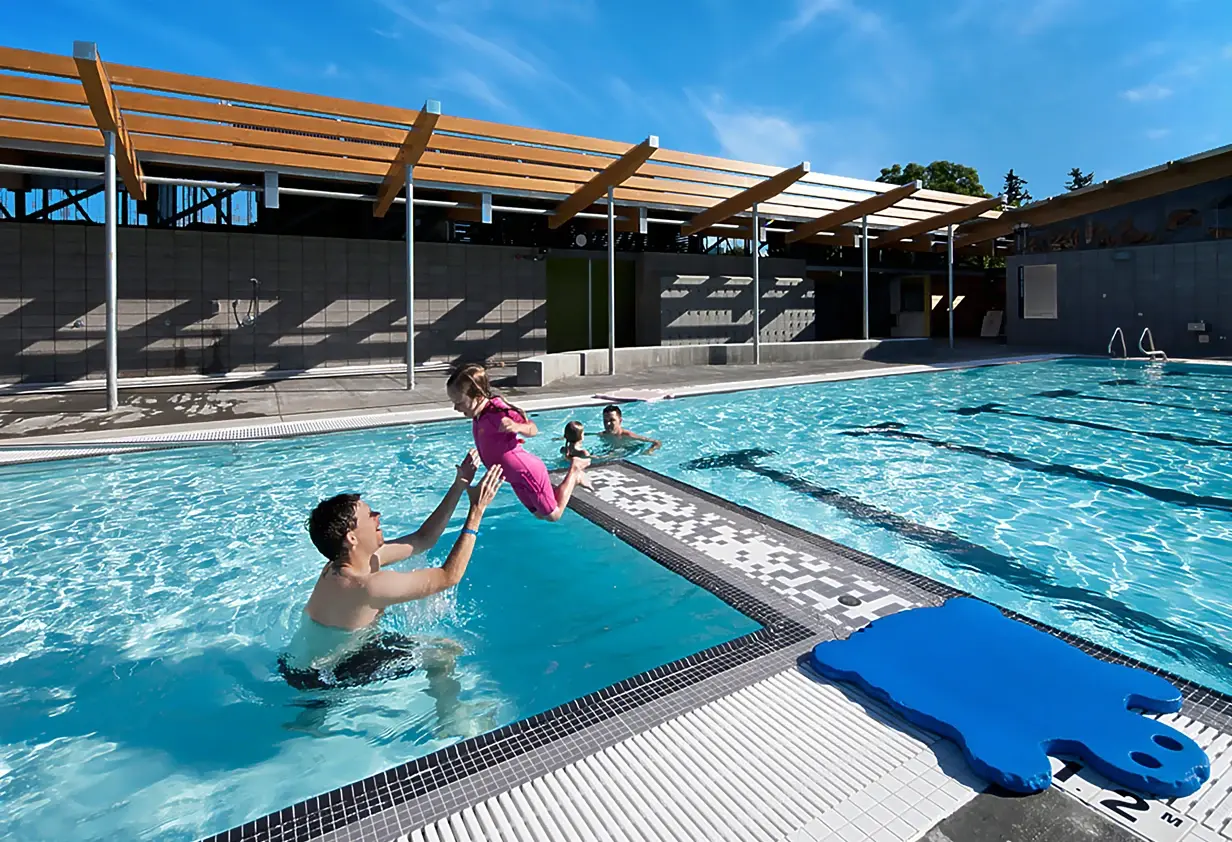 Client-Satisfaction-Image-2025 Young girl jumping into the pool into her dad's arms. JEN COL builds community centres and public municipal places where people can have fun.